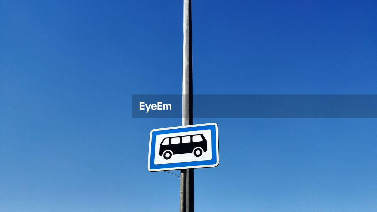 Low angle view of road sign against clear blue sky