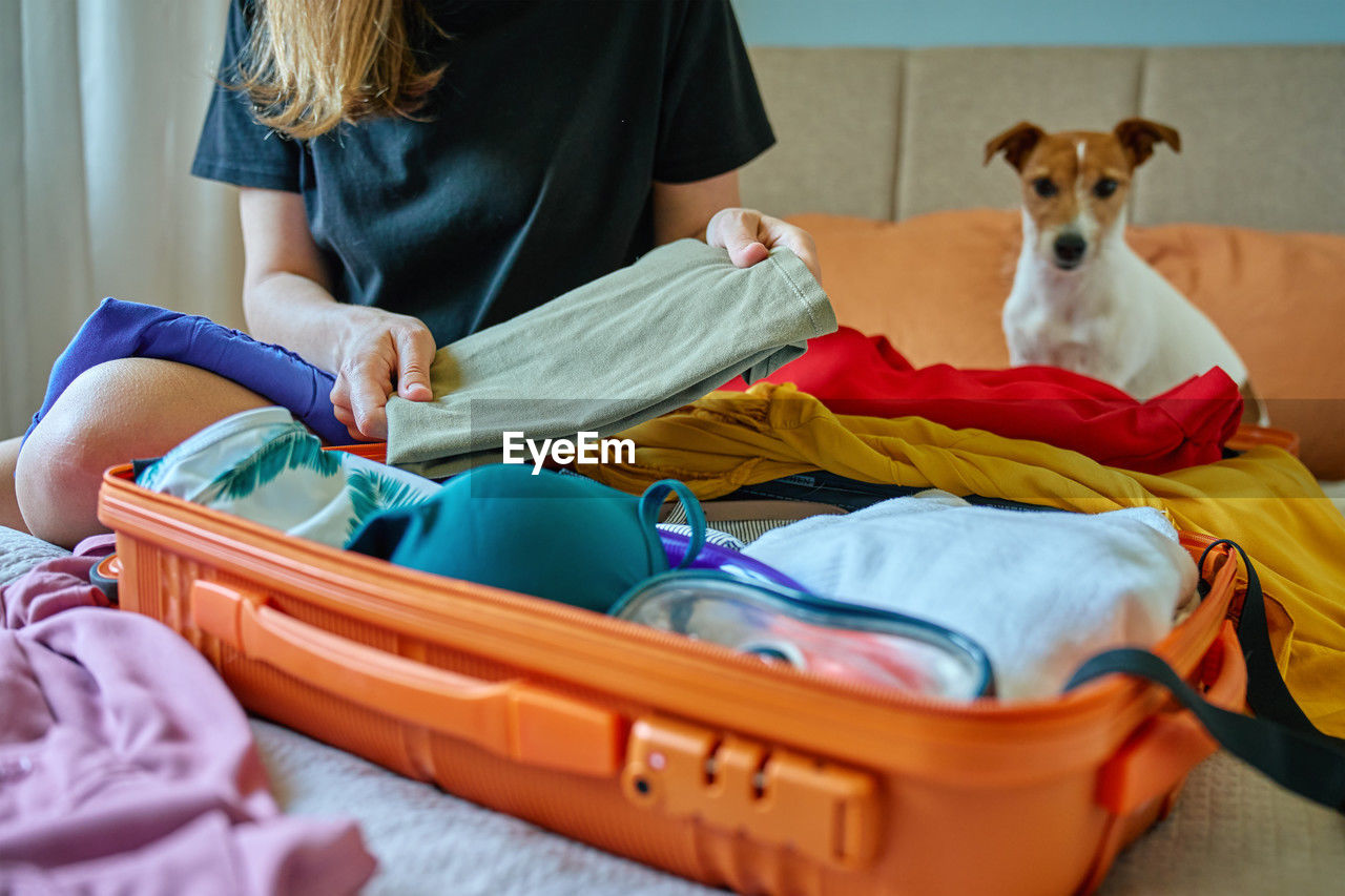 Woman packing colorful clothes into orange suitcase