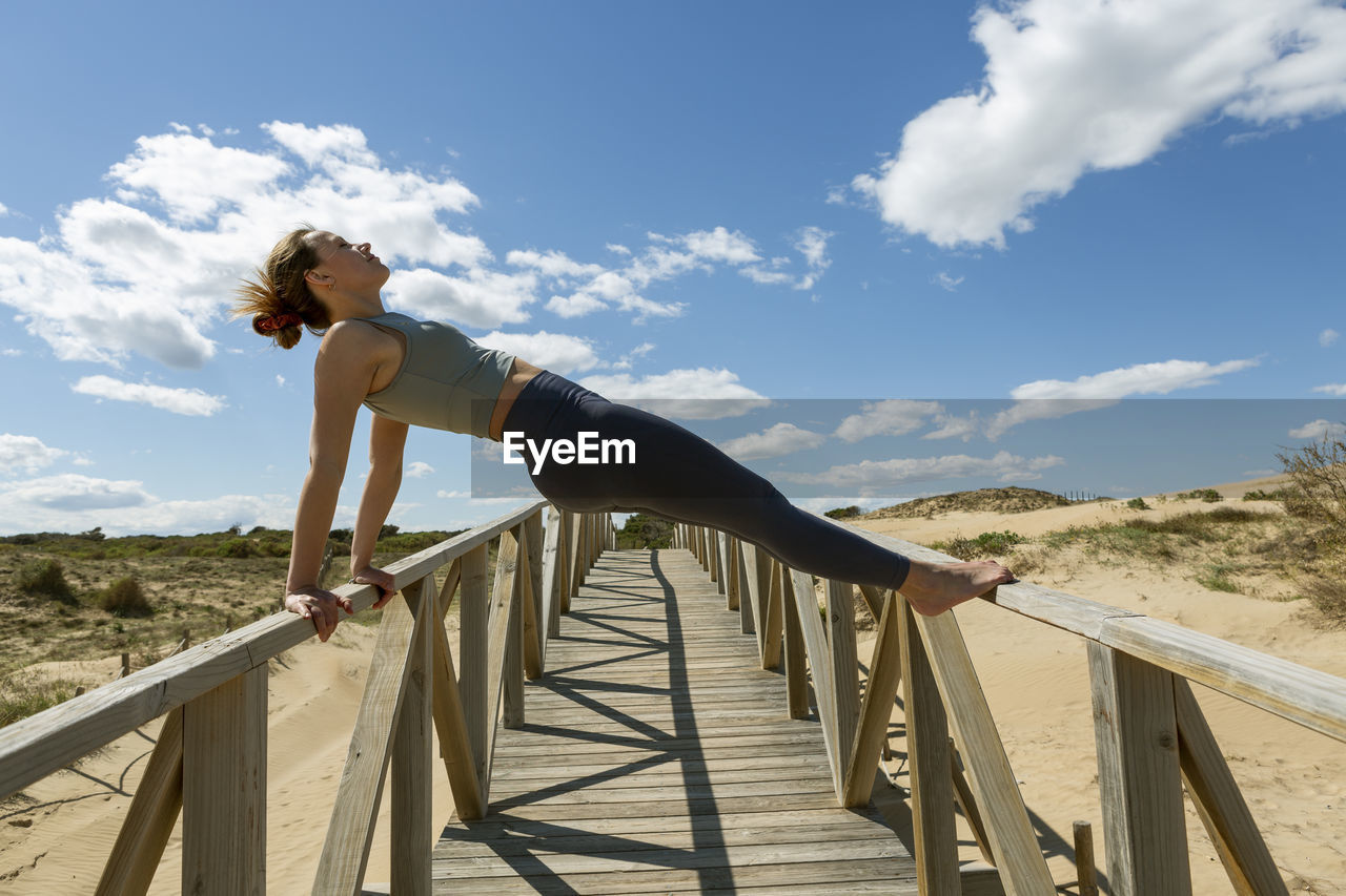 Young woman performing pilates-yoga on a wooden walkway next to the beach