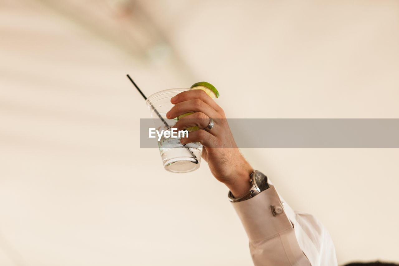 Cropped hand of man holding drink against wall