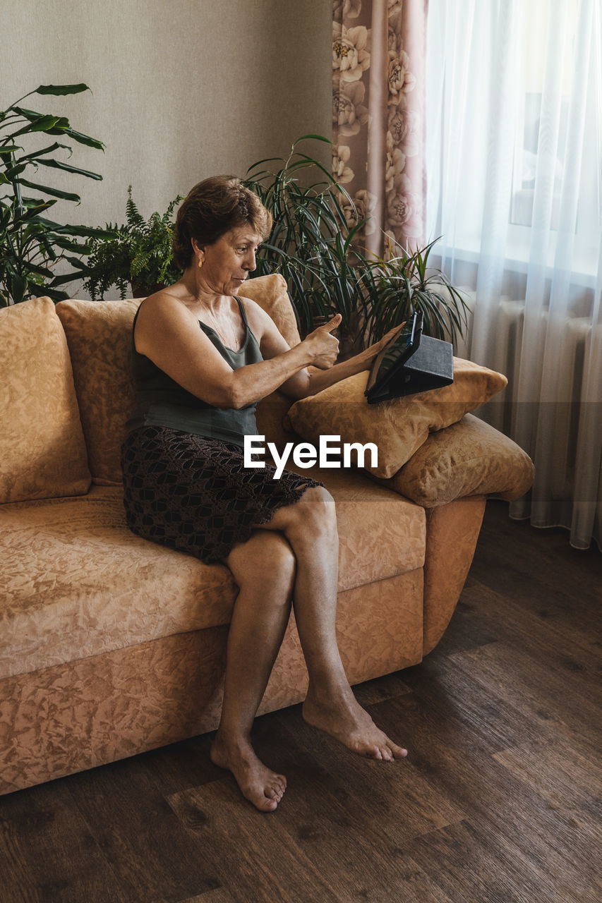 Woman gesturing while holding digital tablet on sofa at home