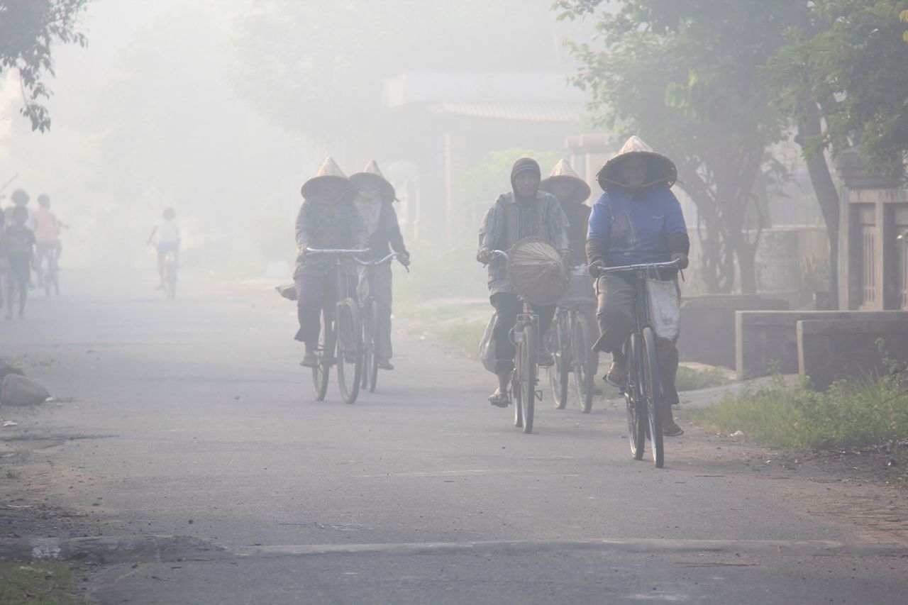 People riding bicycles on street during foggy weather in city