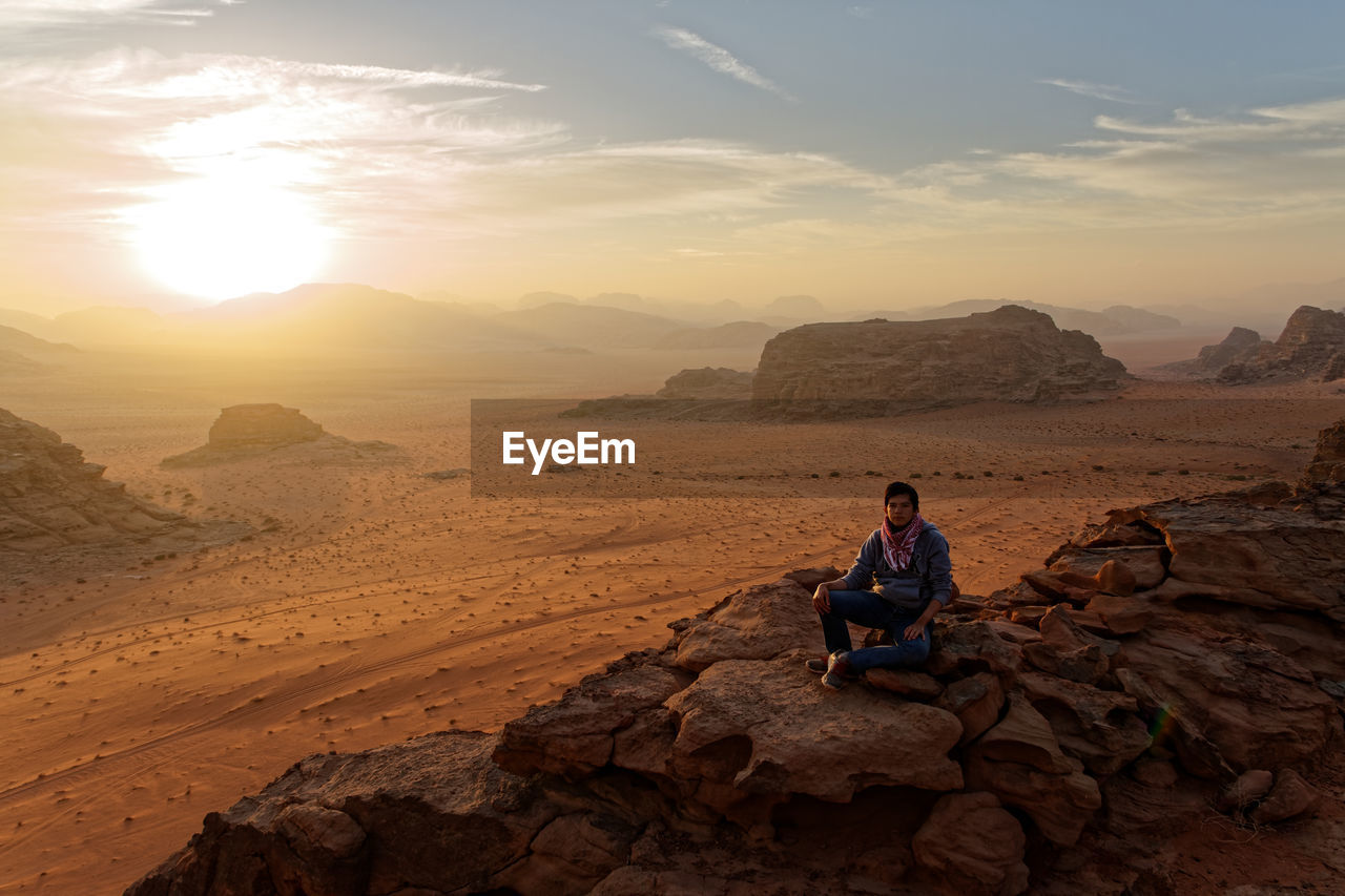 High angle view of teenage boy sitting on rock formation at desert against sky