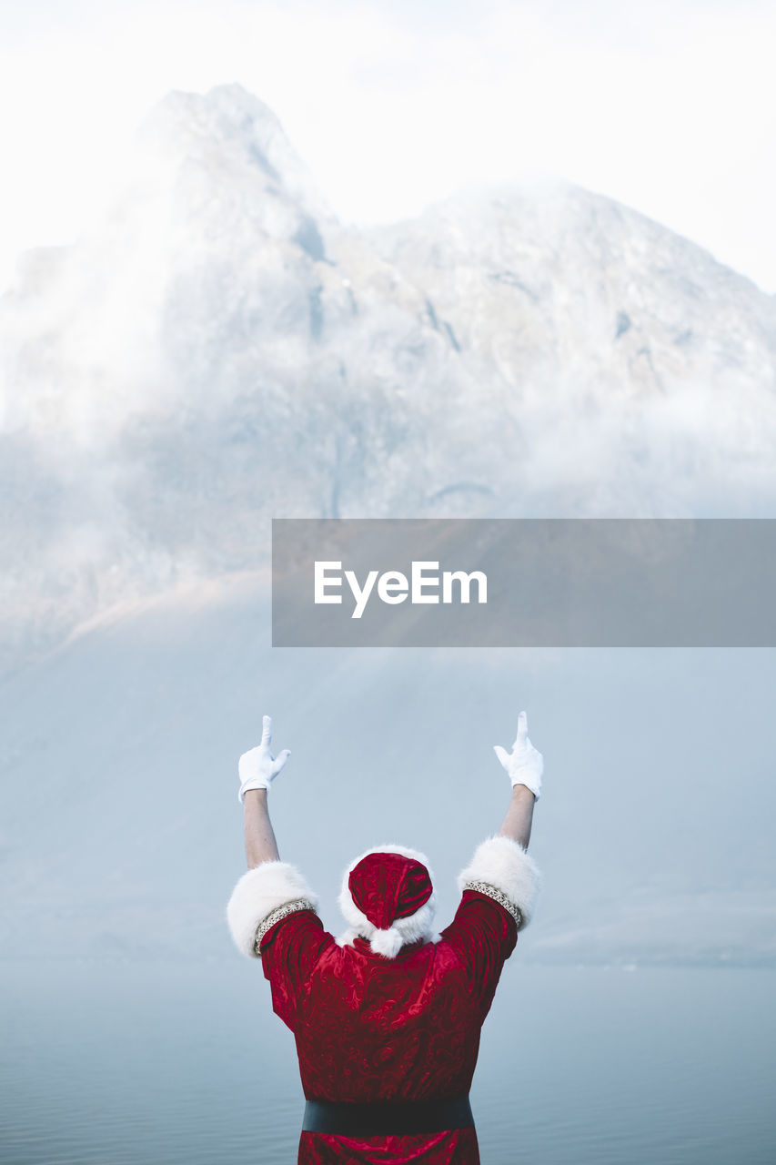 Rear view of man wearing santa claus costume looking at lake during foggy weather