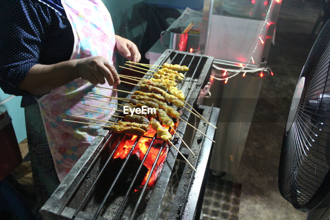 Midsection of woman preparing meat on barbecue grill