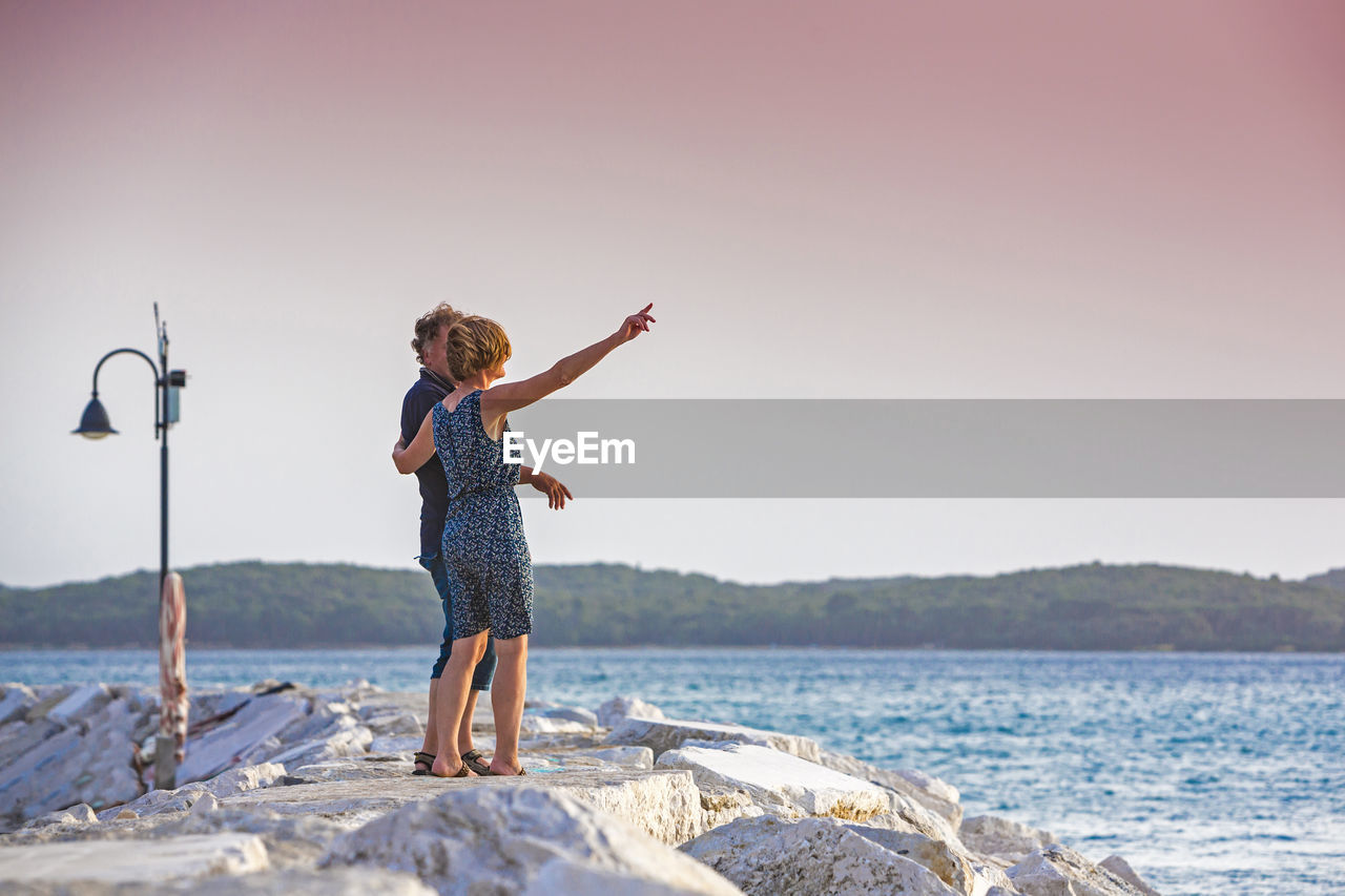 Full length of couple standing on pier by sea against sky