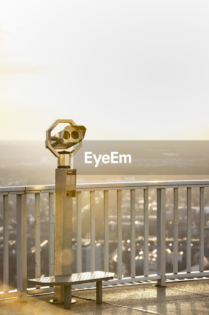 Coin-operated binoculars by railing against clear sky