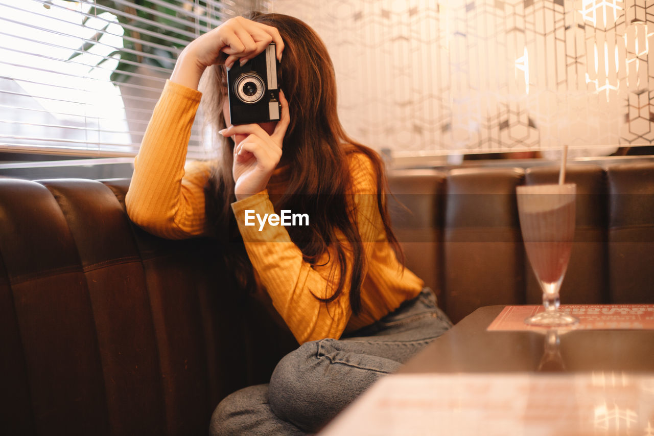 Young woman photographing with vintage camera while sitting in cafe