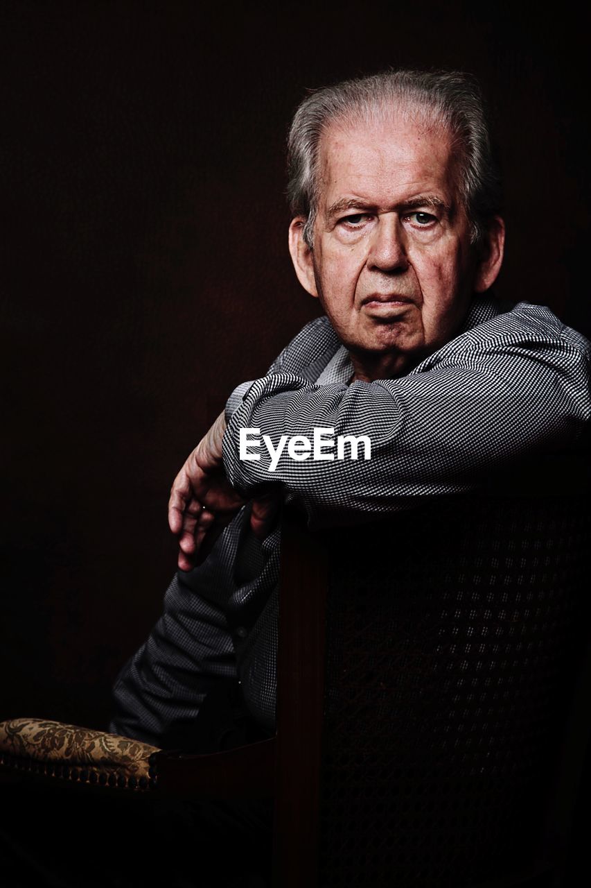 PORTRAIT OF MID ADULT MAN SITTING AGAINST BLACK BACKGROUND