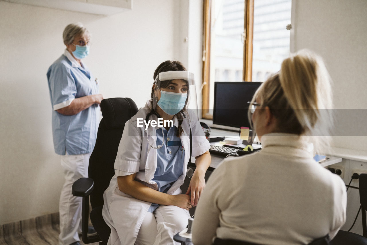 Female healthcare worker wearing mask and face shield talking patient in medical clinic