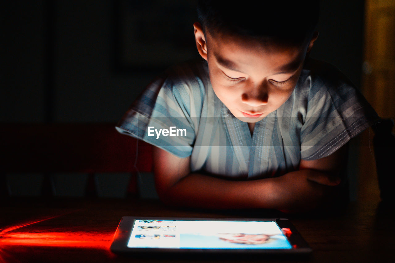 Boy sitting and looking at an ipad on table in the dark