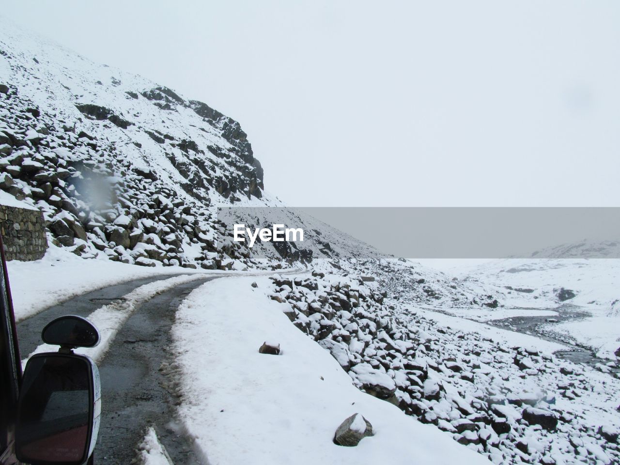 Cropped image of car on snow covered mountain road against clear sky
