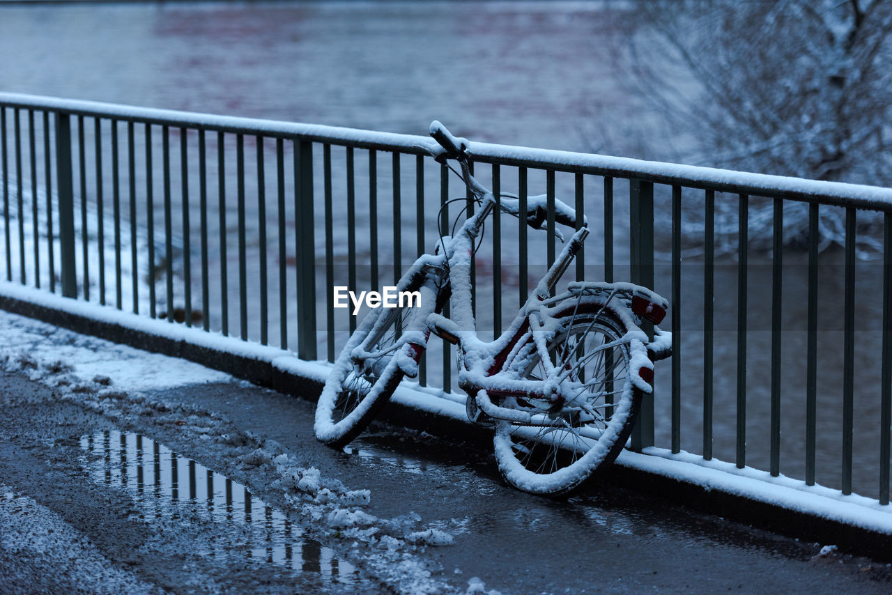 BICYCLE ON RAILING BY SNOW COVERED BRIDGE