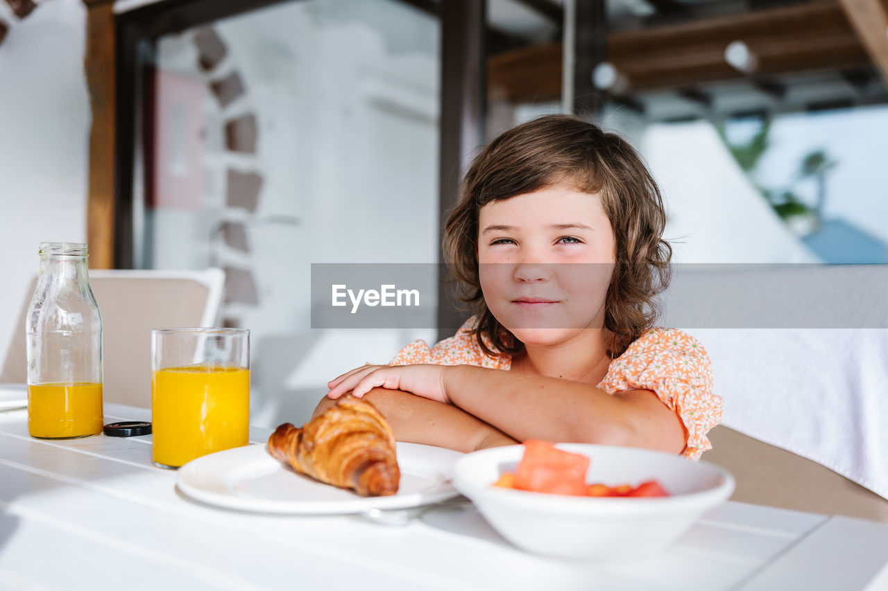 Delightful preschool kid looking at camera while sitting at table with food in cafeteria