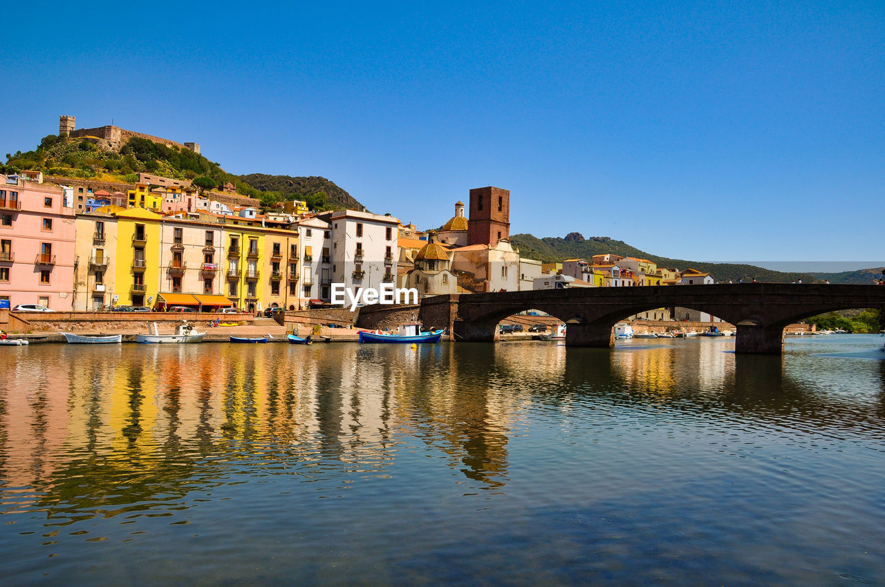 Arch bridge over river against clear blue sky in city