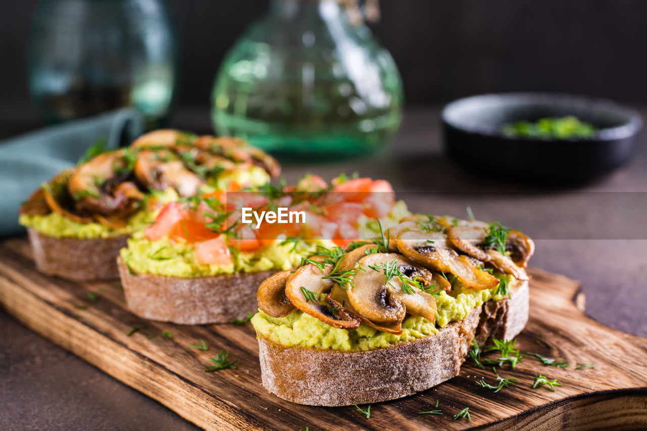 Sandwiches with avocado, fried champignons, tomatoes and herbs on rye bread on a board