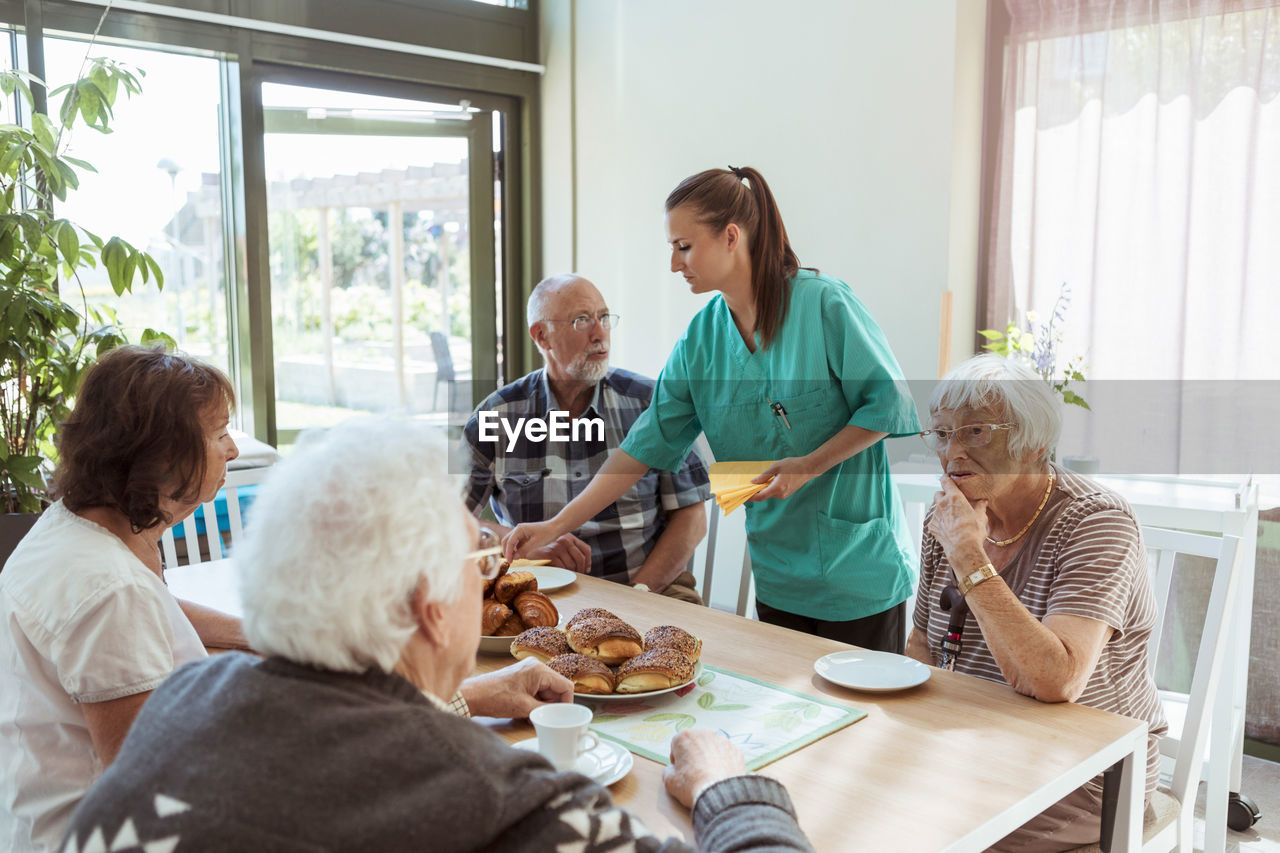 Elderly care nurse serving meal to people at table in nursing home