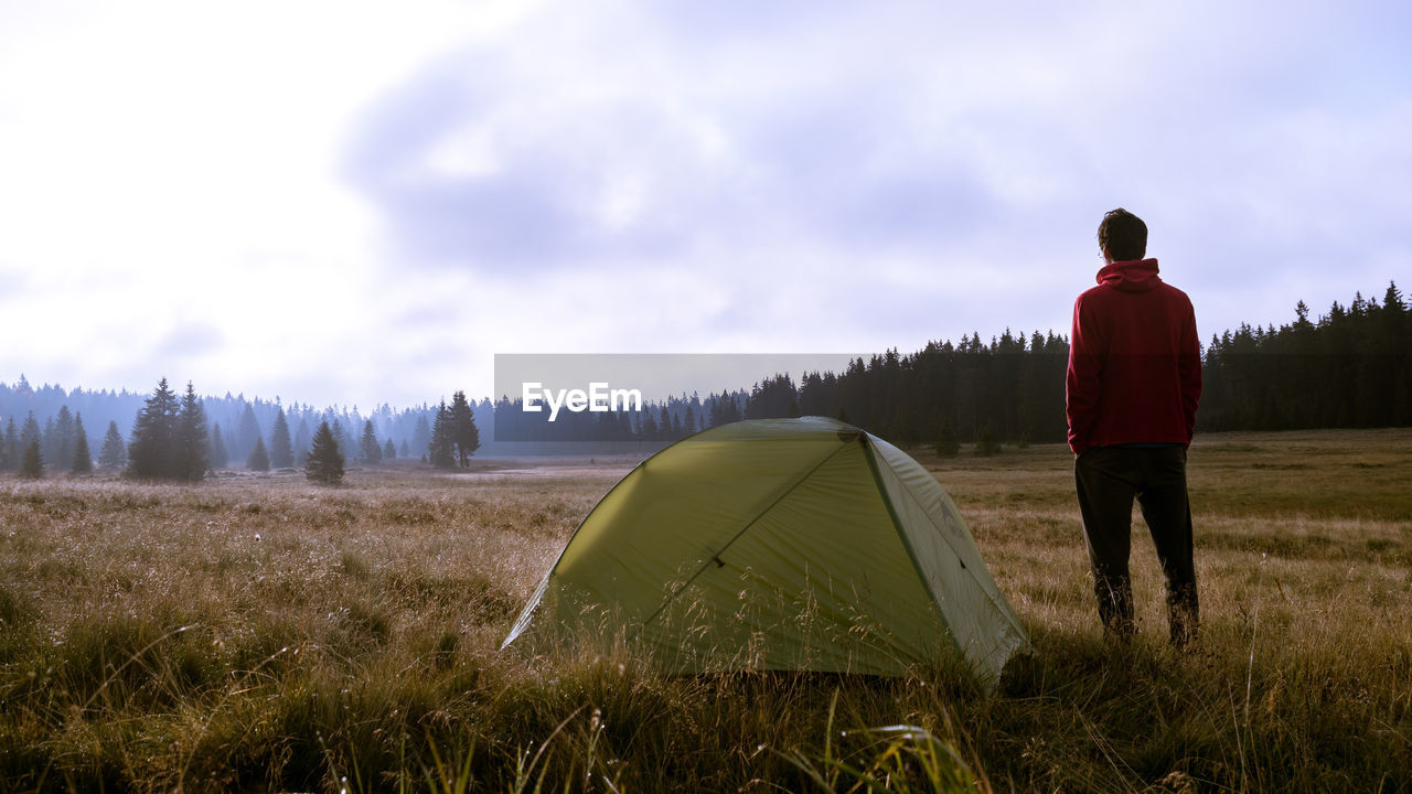 Rear view of man standing by tent on land against sky