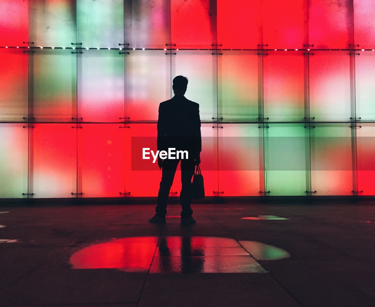 Silhouette man standing against illuminated wall at night