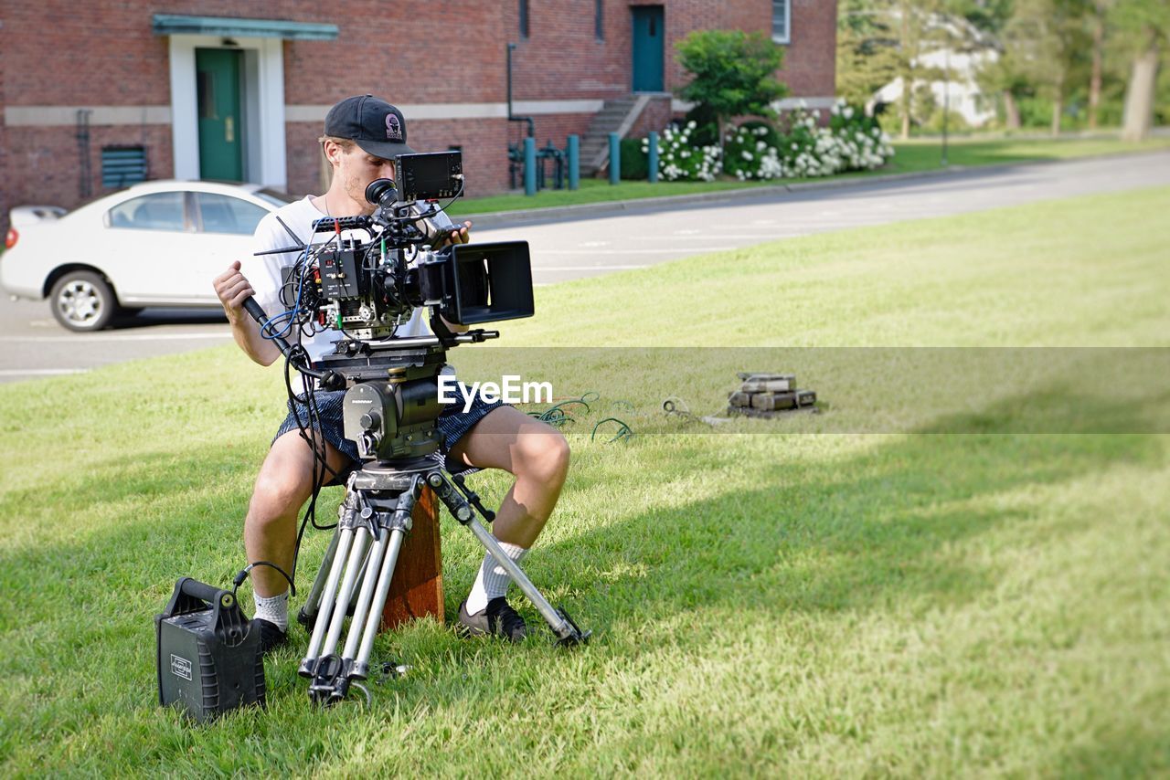 MAN PHOTOGRAPHING CAMERA ON GRASS