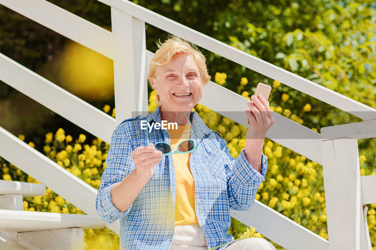 Mature woman sitting alone on the terrace of beach cafe and using mobile phone