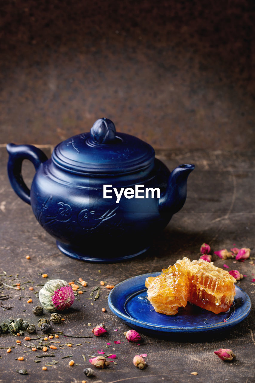 Teapot by honeycombs in plate with roses on floor