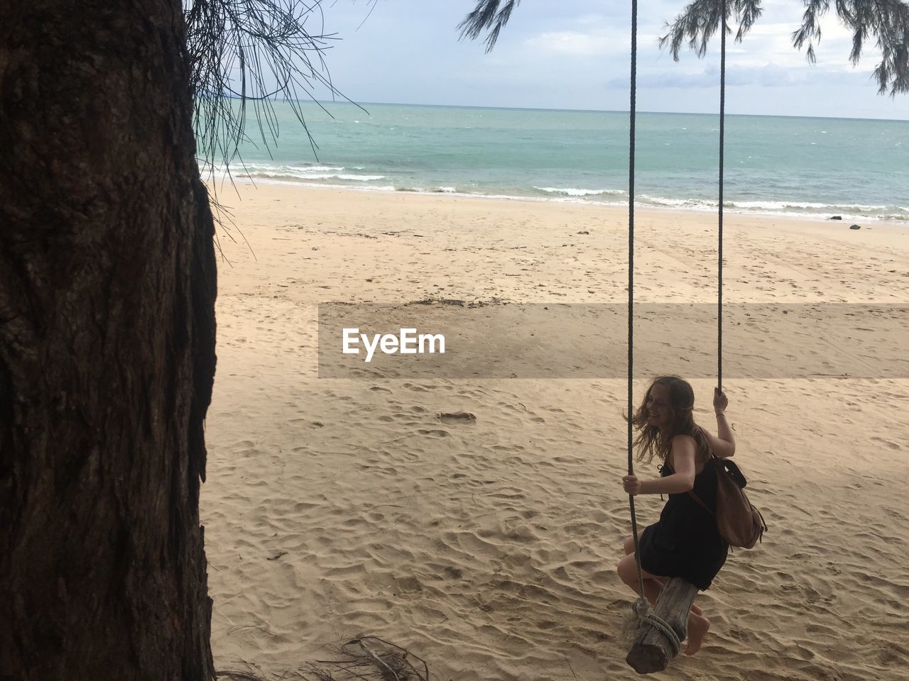 FRIENDS STANDING ON TREE TRUNK BY SEA