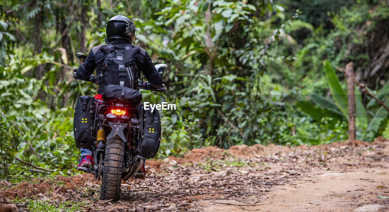 Woman riding her scrambler type motorcycle through forrest