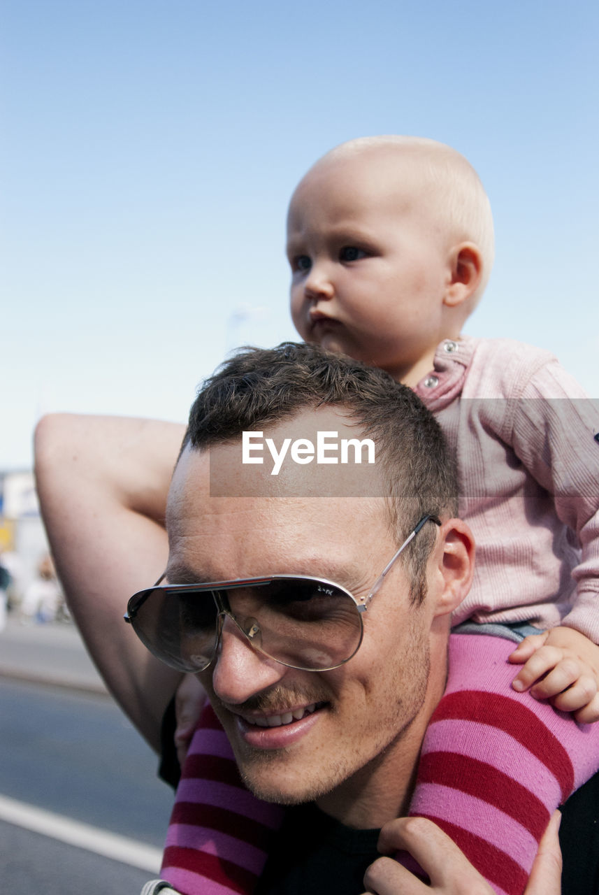 Close-up of father carrying son on shoulder against clear sky