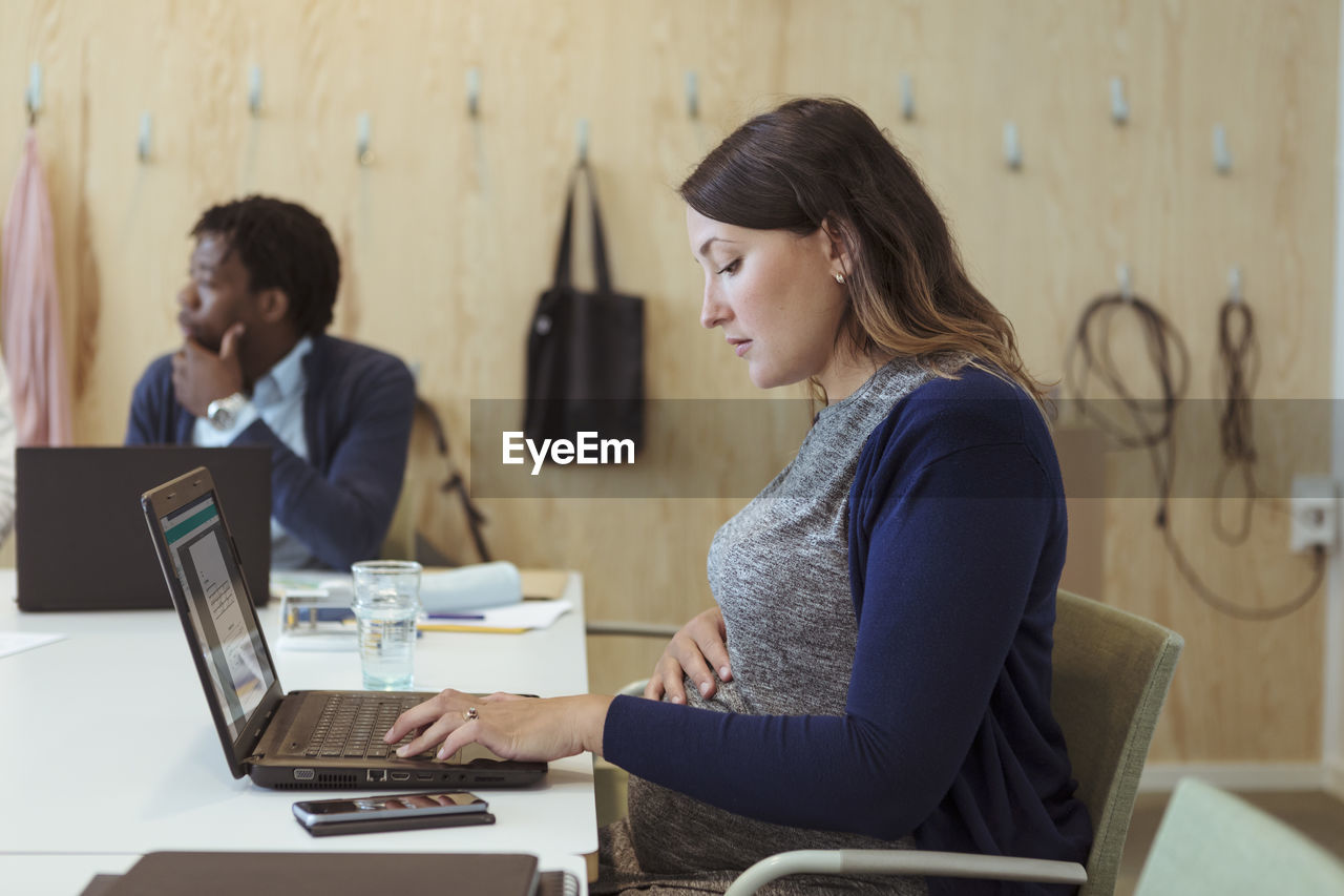 Side view of pregnant businesswoman using laptop at conference table in office