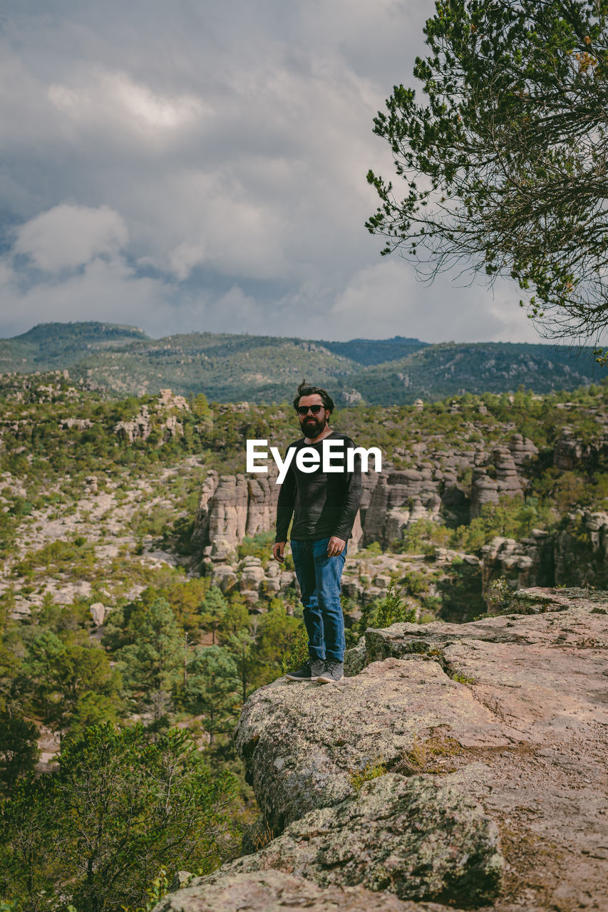 PORTRAIT OF WOMAN STANDING ON ROCK AGAINST SKY