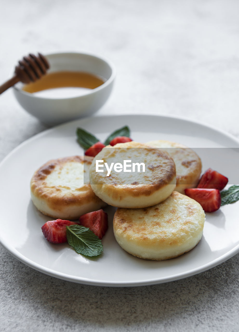 Cottage cheese pancakes, ricotta fritters on ceramic plate with fresh strawberry. 