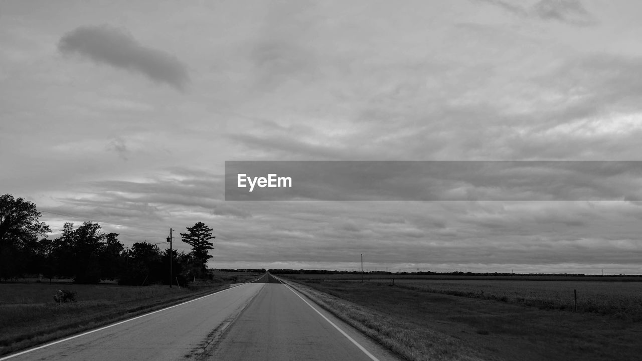 Empty road amidst field against sky