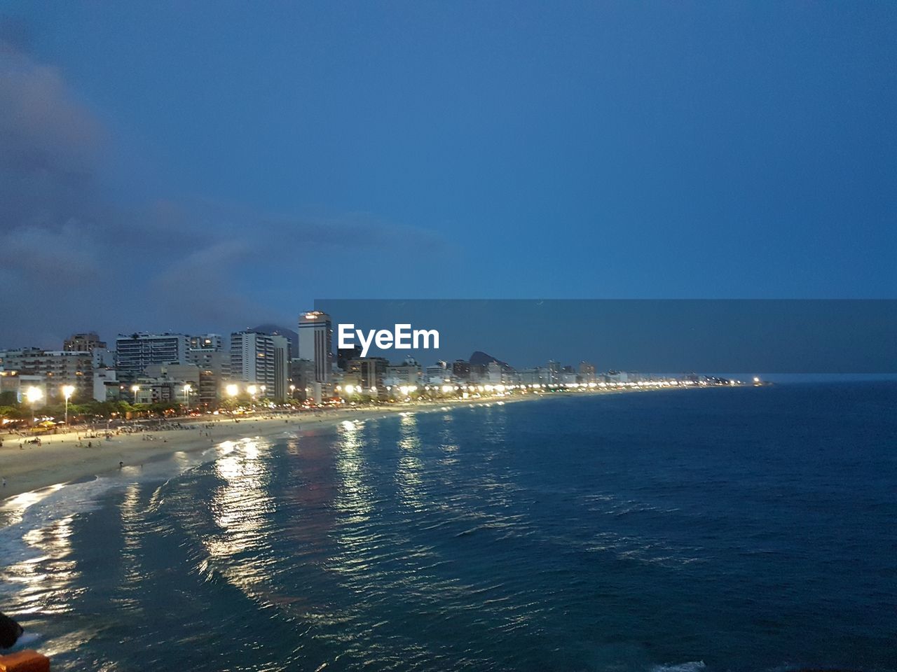 ILLUMINATED CITYSCAPE BY SEA AGAINST SKY