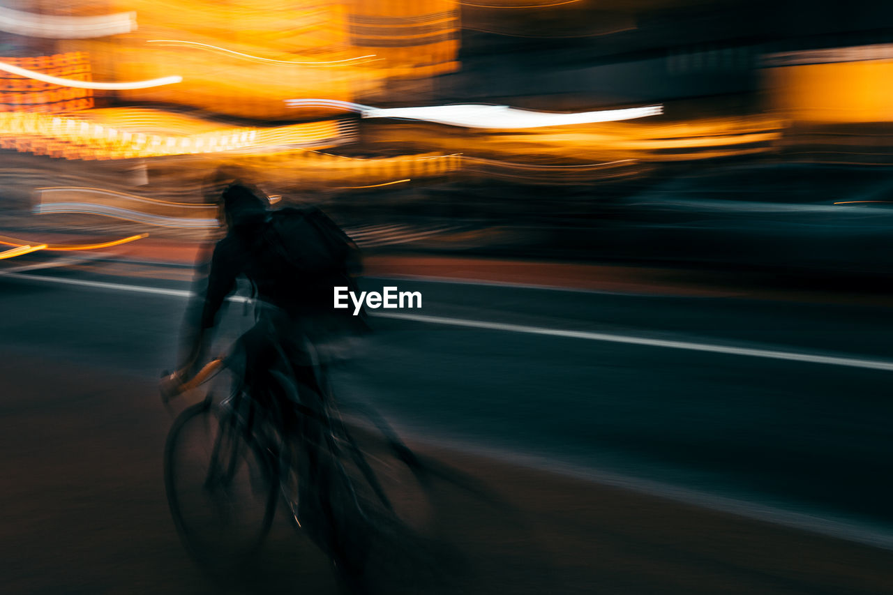 Blurred motion of person riding bicycle on road at night