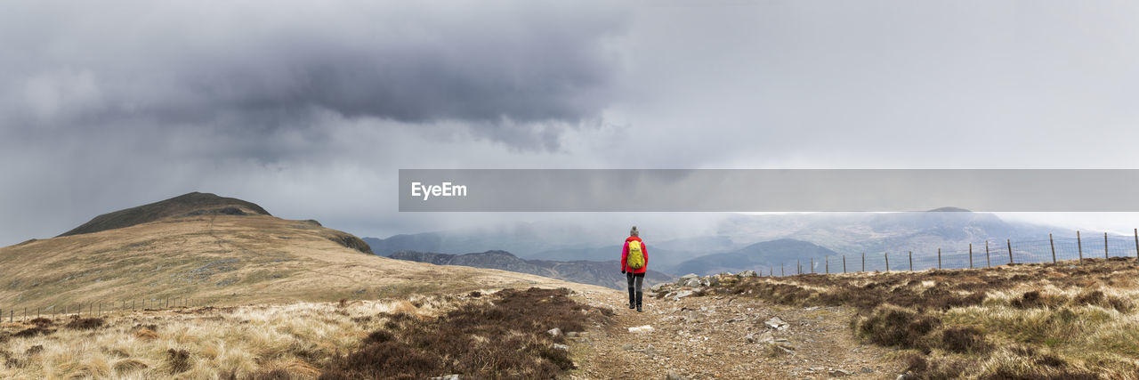 Active senior woman with backpack hiking on mountain under cloudy sky