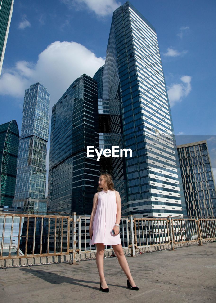 Full length of woman standing against modern buildings in city against sky