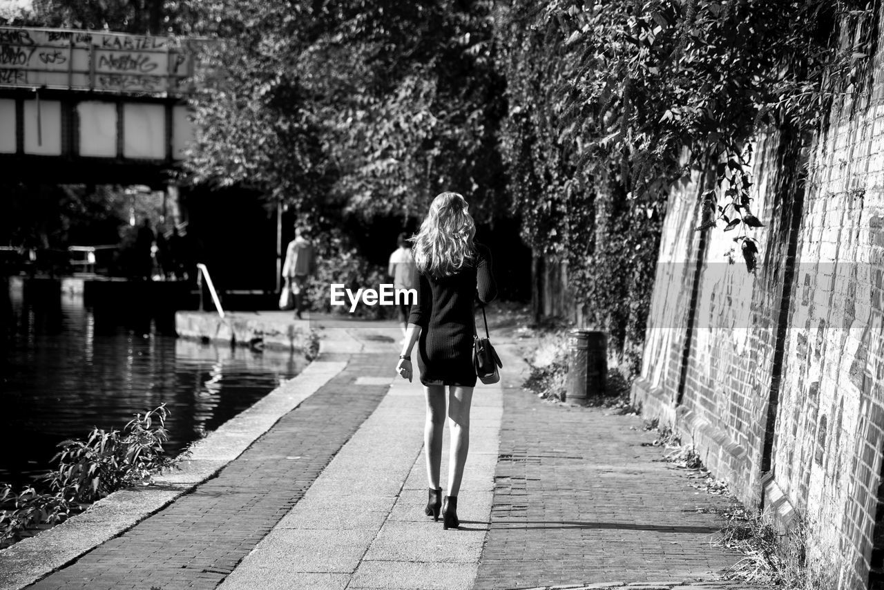 Rear view of woman walking on footpath by canal