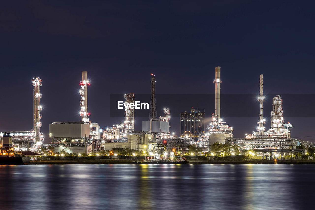 Oil refinery at night petrochemical and energy industry with refection on river