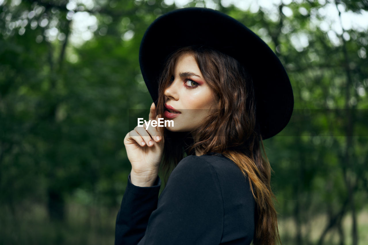 portrait of young woman looking away against trees