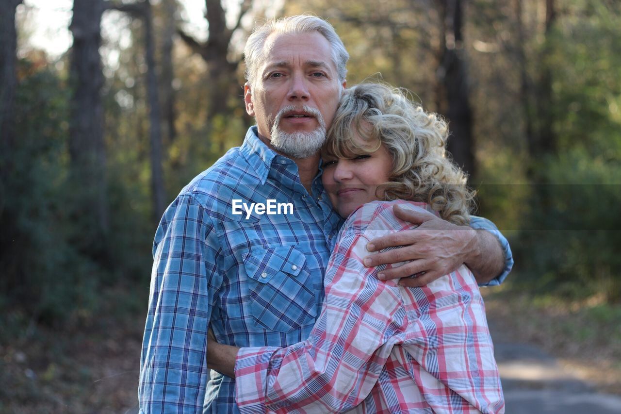 Portrait of mature couple embracing while standing in forest