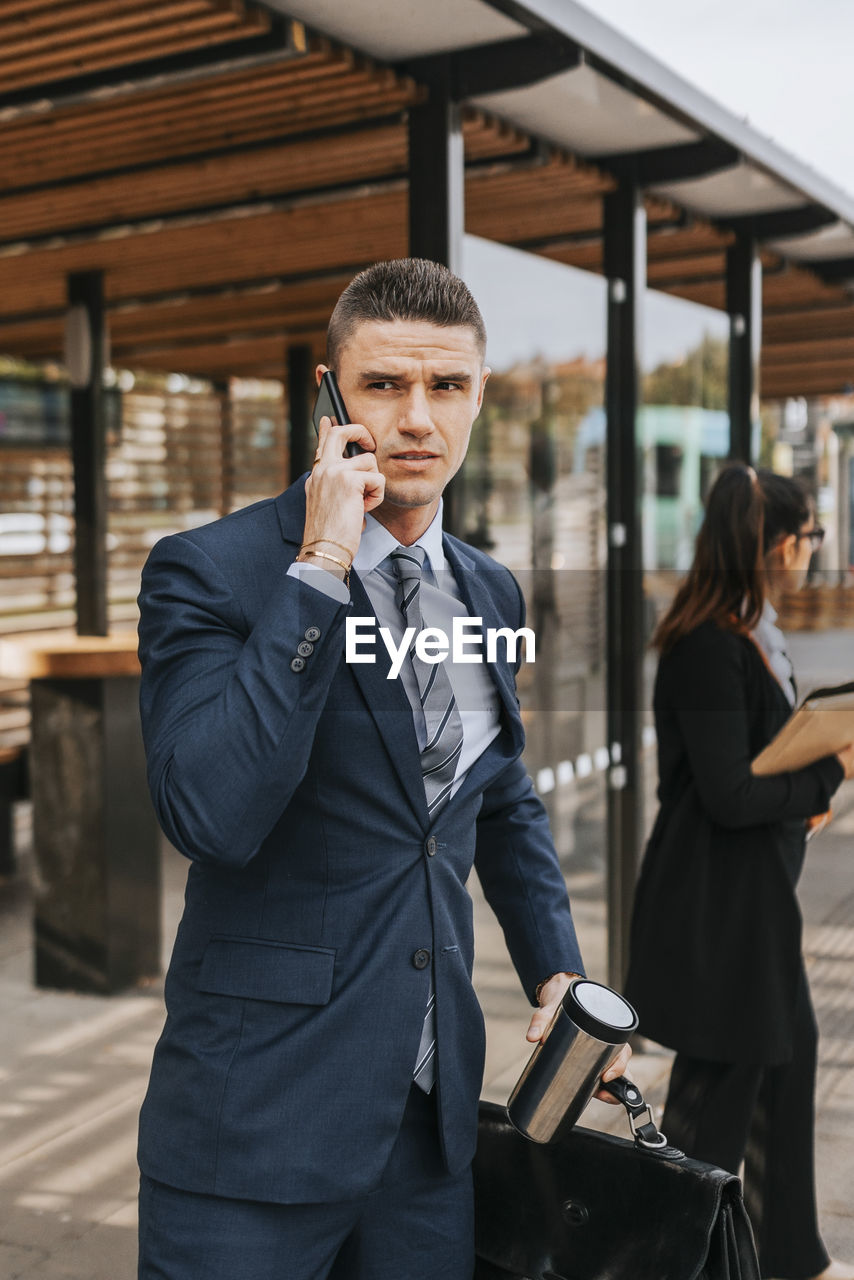 Businessman talking on smart phone while waiting at bus stop