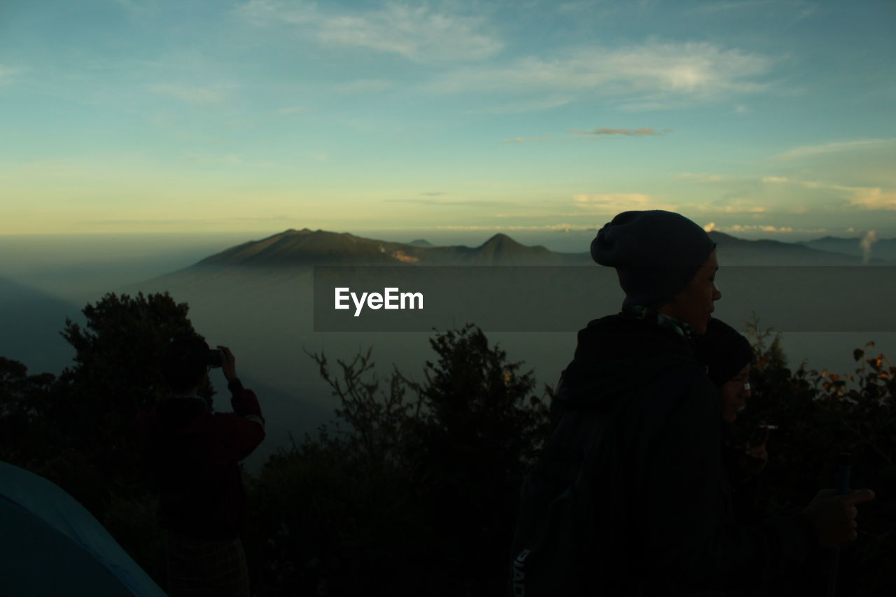 Rear view of silhouette friends against mountains during sunset