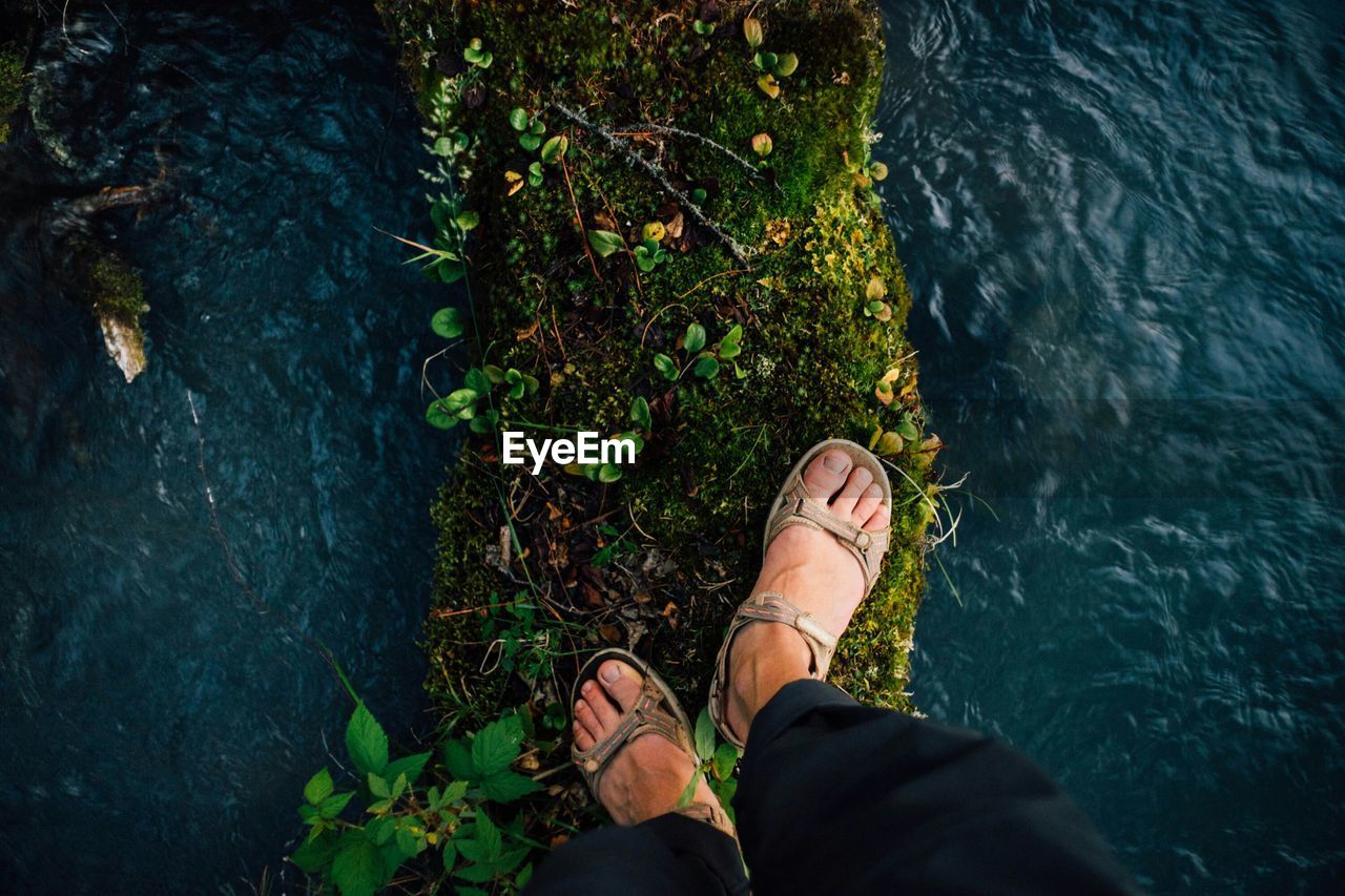 Low section of person standing on moss covered retaining wall amidst lake