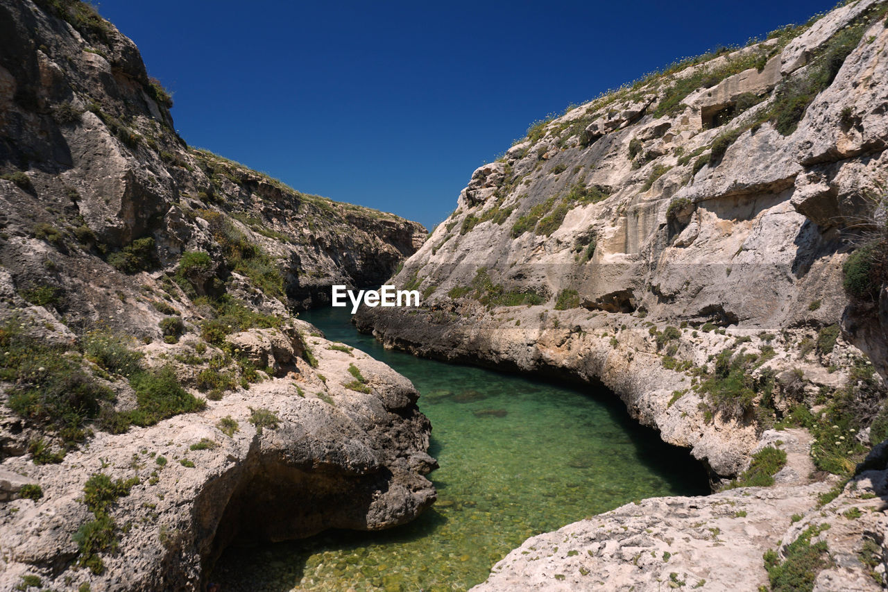 Rock formation by river against clear blue sky