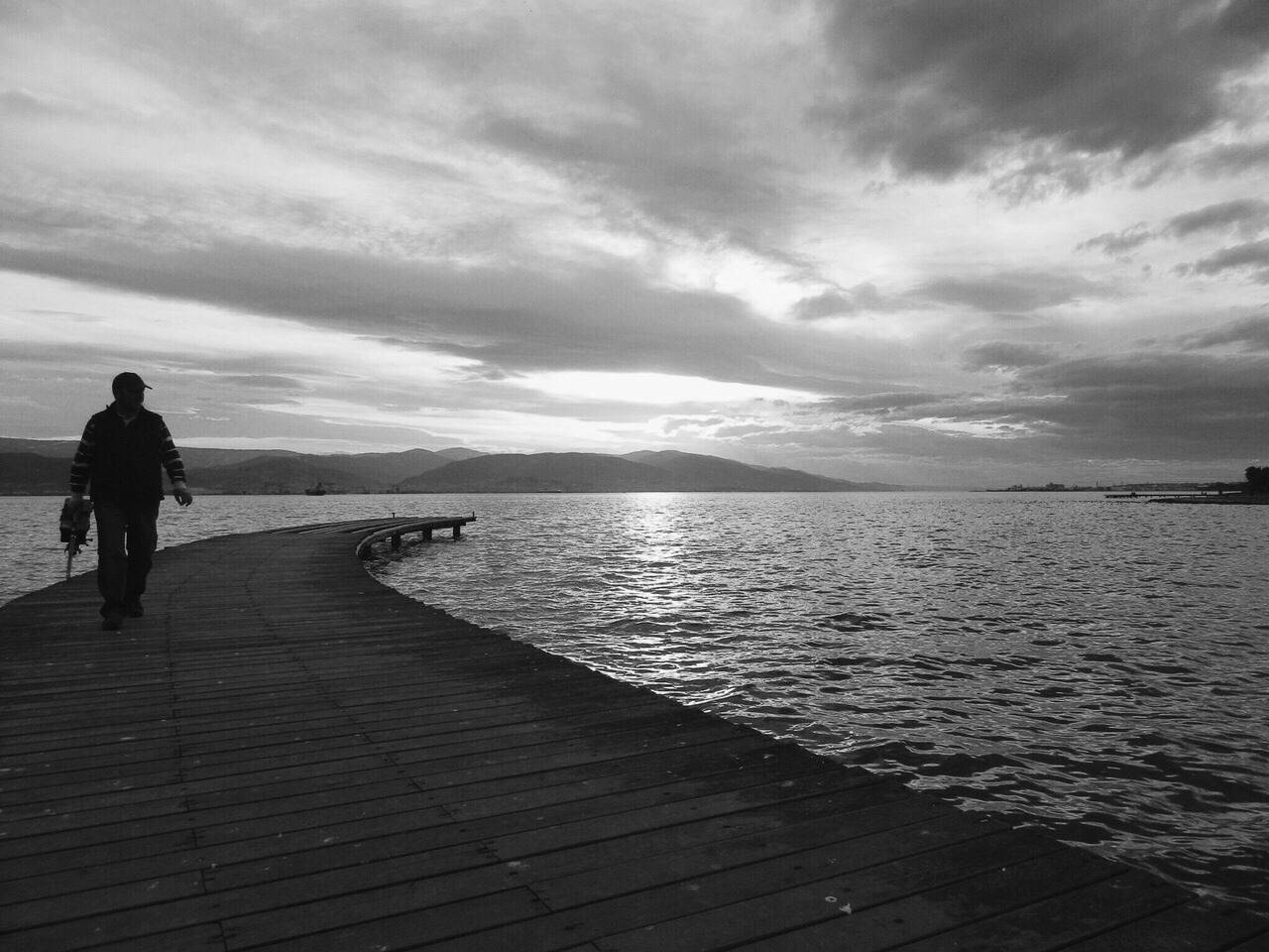 Boardwalk leading towards river against cloudy sky