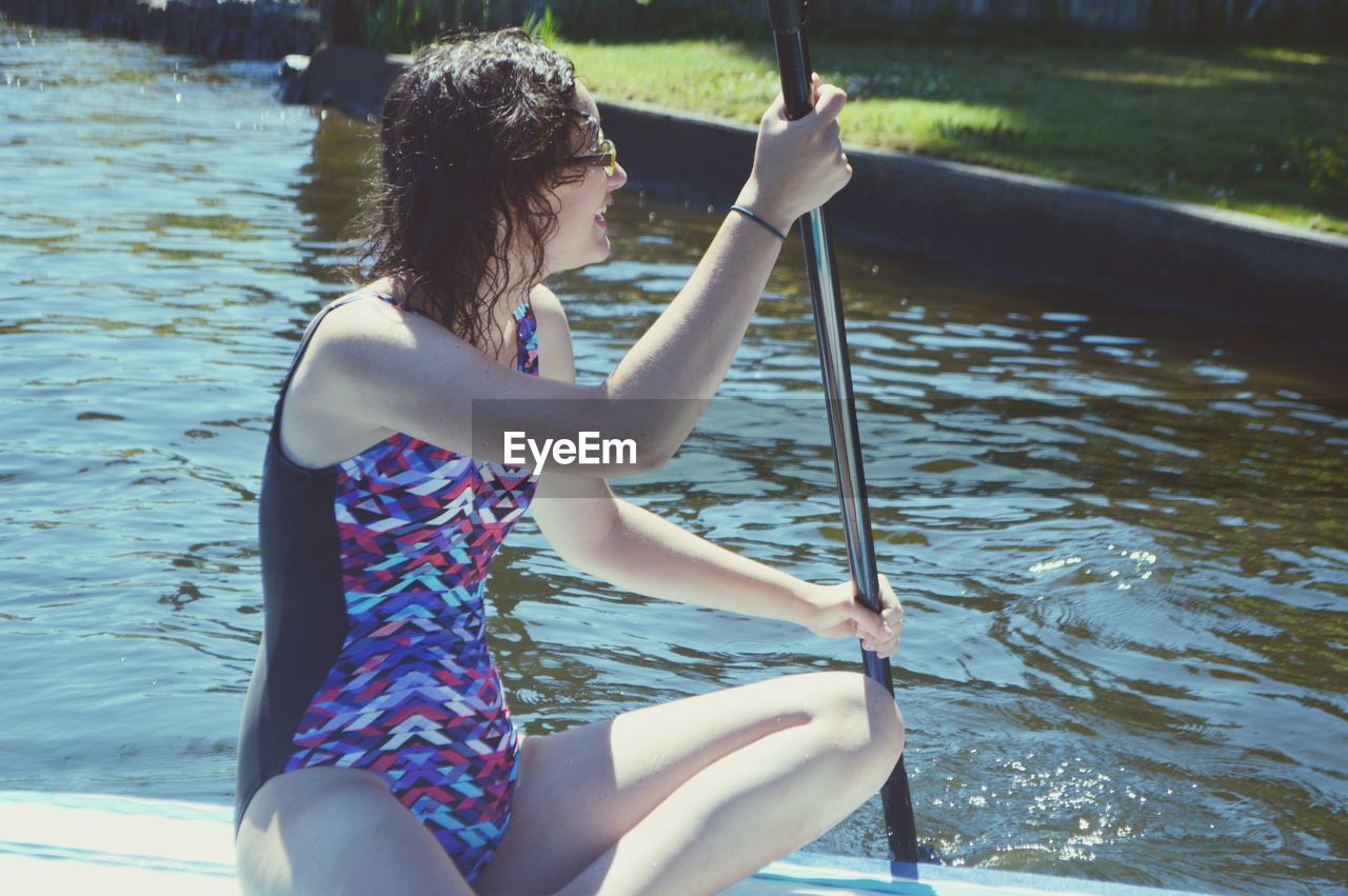 REAR VIEW OF YOUNG WOMAN SITTING ON RIVER