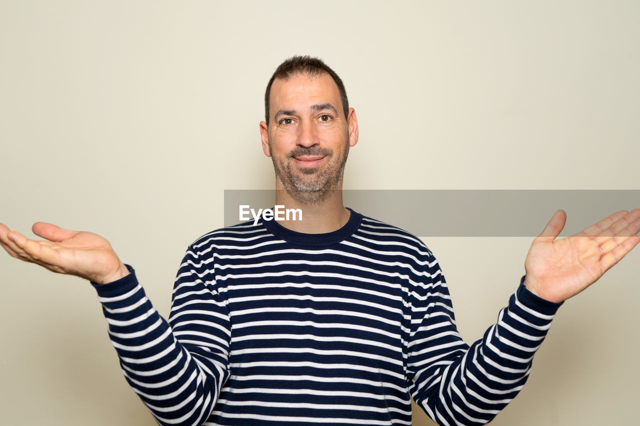 one person, striped, adult, portrait, men, studio shot, finger, gesturing, casual clothing, looking at camera, smiling, indoors, waist up, happiness, emotion, hand, sign language, arm, front view, limb, facial hair, positive emotion, beard, standing, human limb, person, cheerful, copy space, young adult, t-shirt, thumbs up, colored background, hand sign, sitting, pointing, communication, brown hair, success
