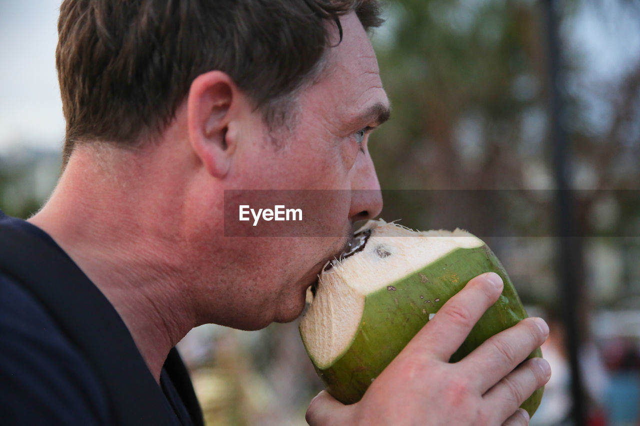 Side view of man drinking coconut water