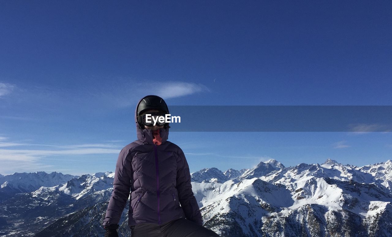 YOUNG MAN STANDING ON SNOWCAPPED MOUNTAIN AGAINST SKY